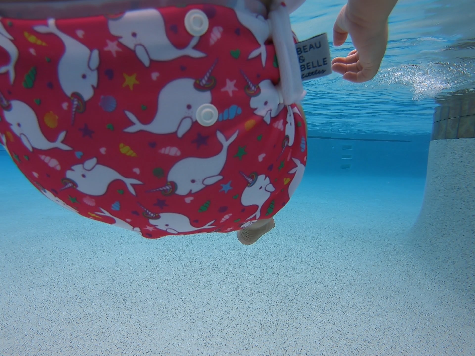 underwater image of a Beau and Belle Littles Swim Diaper, Larger Size, dark pink background, narwhals 
