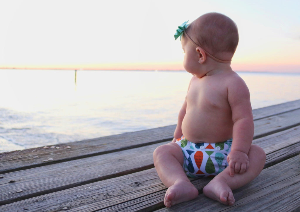 bald baby girl sitting on a dock wearing a Beau and Belle Littles Swim Diaper, Regular Size, fish print