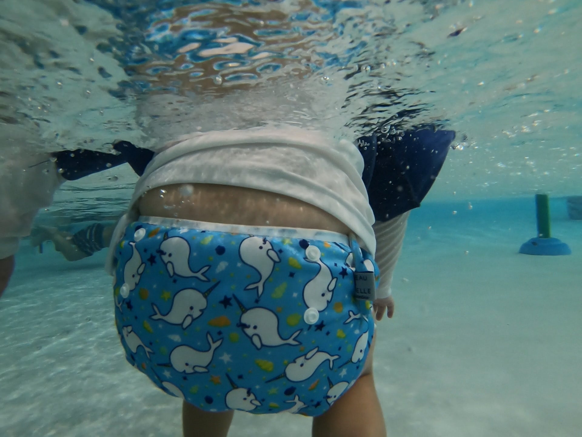 underwater image of a toddler wearing a Beau and Belle Littles Swim Diaper, Larger Size, light blue background, narwhals 