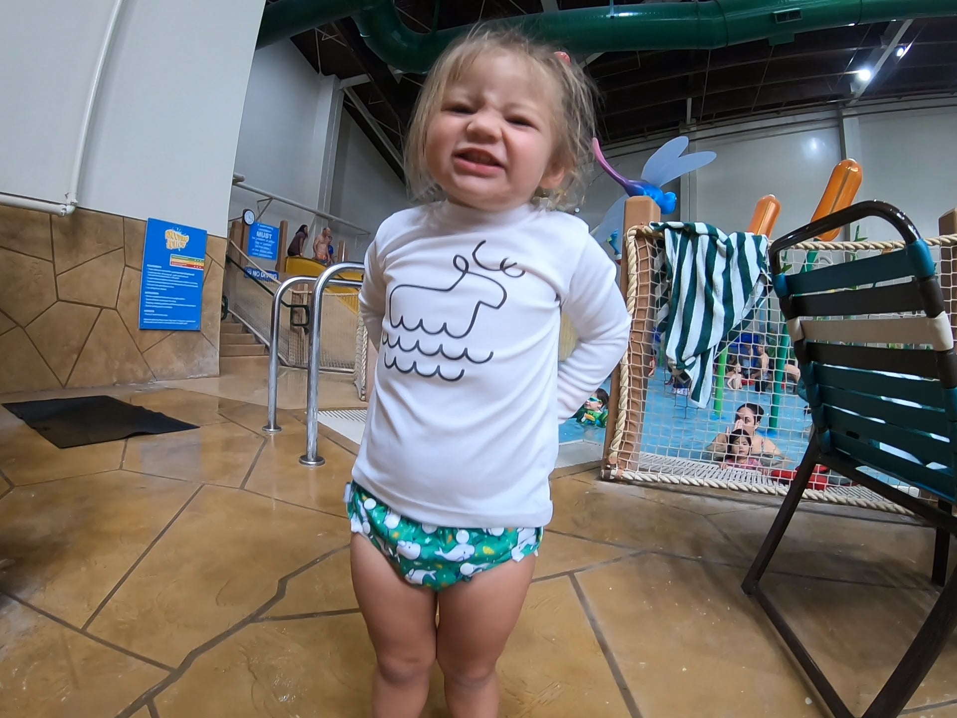 toddler girl at an indoor pool wearing a Beau and Belle Littles Swim Diaper, Regular Size, green background, narwhals 