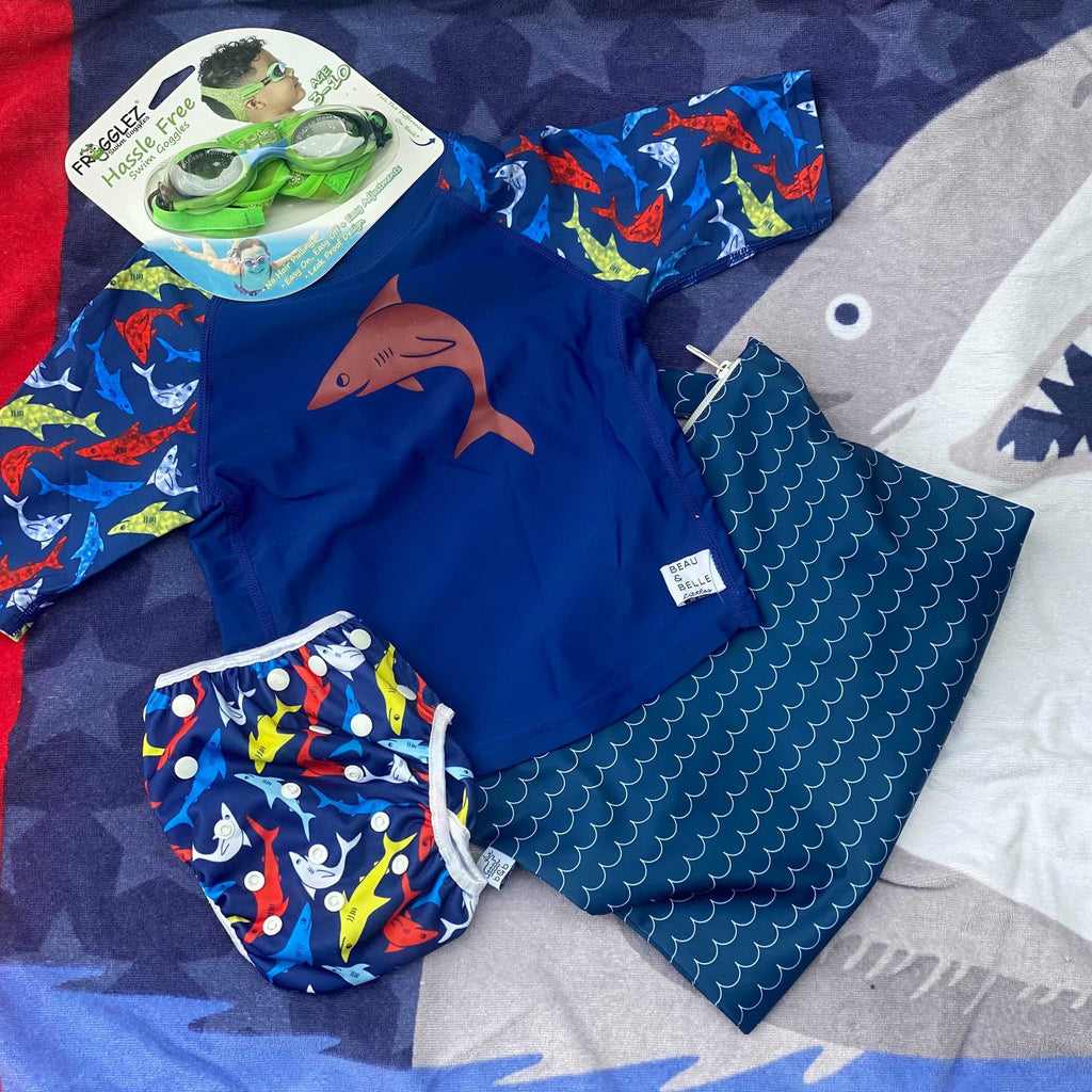 swimming starter kit for boys with blue colorful sharks designs. This kit includes green Frogglez Goggles, a blue waves wet bag, shark swim bottom with a diaper included, and a matching swim shirt