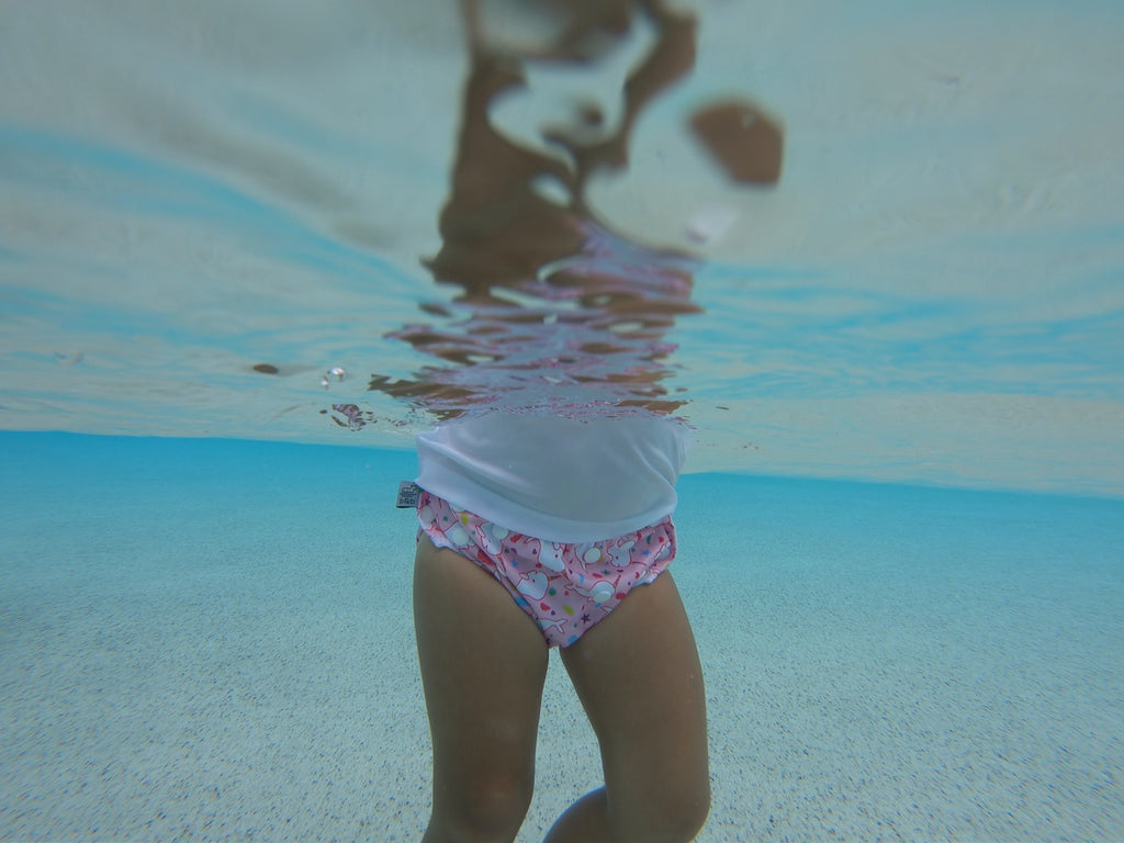 underwater image of a toddler wearing a Beau and Belle Littles Swim Diaper, Regular Size, light pink background, narwhals 