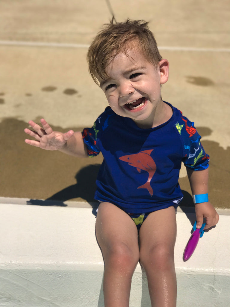 happy boy wearing a Beau and Belle Littles Rash Guard/Swim Shirt, dark blue with lighter blue 3/4 sleeves, shark print and matching swim diaper