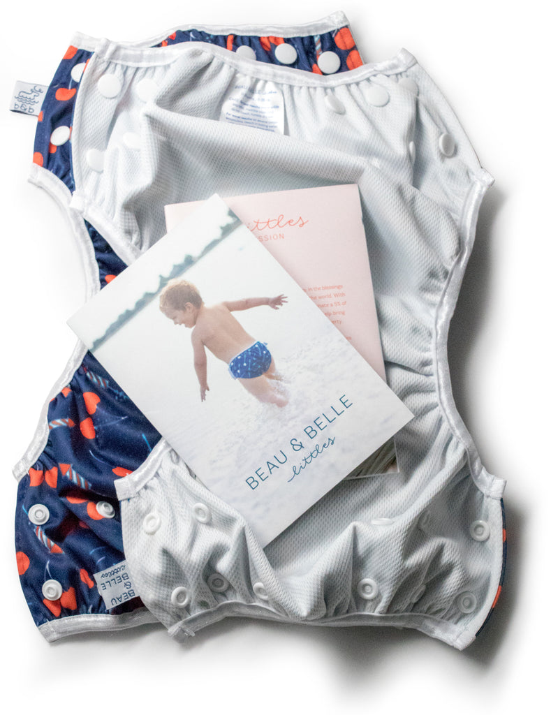 Beau and Belle Littles Swim Diaper, Regular Size, Lauren Holiday Cherry bomb print - two layered on top of each other to show the outside print and the inner lining. The image also includes the inserts included in the packaging.