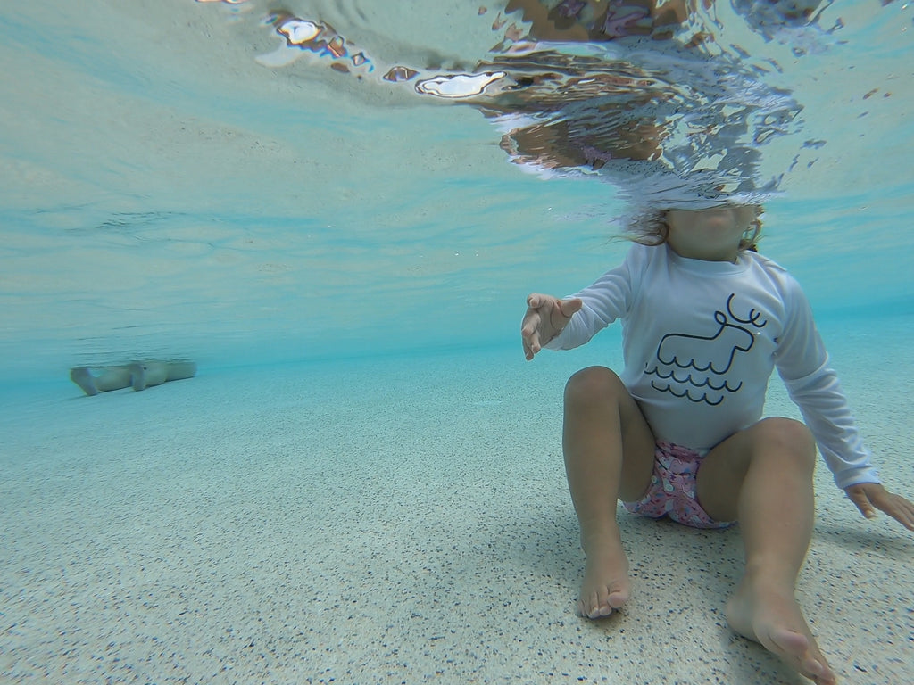 underwater image of a toddler wearing a Beau and Belle Littles Swim Diaper, Regular Size, light pink background, narwhals 